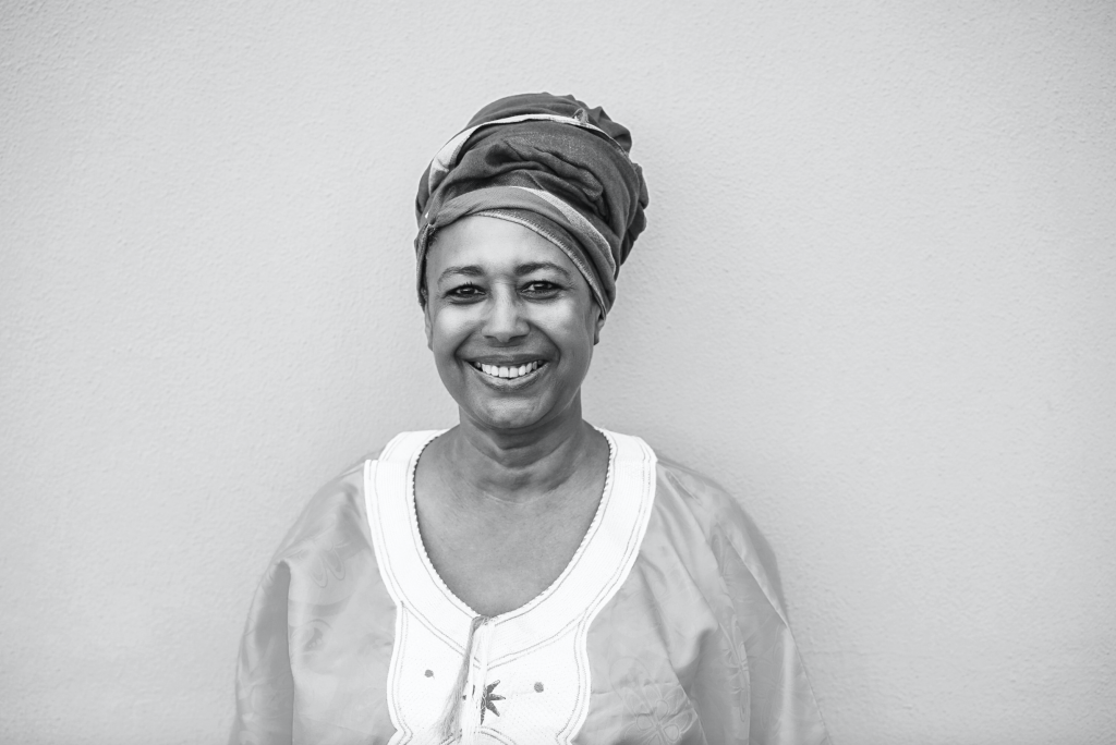 An older black woman smiles confidently at the camera. The image is in black and white.
